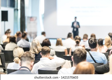 Business And Entrepreneurship Symposium. Speaker Giving A Talk At Business Meeting. Audience In Conference Hall. Rear View Of Unrecognized Participant In Audience.