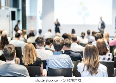 Business and entrepreneurship symposium. Speaker giving a talk at business meeting. Audience in conference hall. Rear view of unrecognized participant in audience. - Shutterstock ID 1476787472