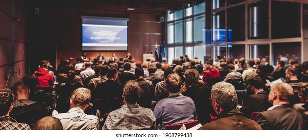 Business and entrepreneurship symposium. Speaker giving a talk at business meeting. Audience in conference hall. Rear view of unrecognized participant in audience. - Shutterstock ID 1908799438