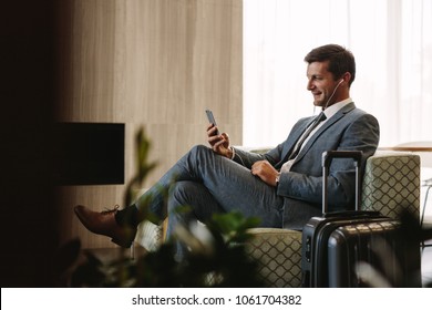 Business Executive Making A Video Call By Mobile Phone While Waiting For His Flight. Businessman At Airport Lounge Doing A Video Conference Call From His Smart Phone.