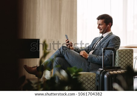 Business executive making a video call by mobile phone while waiting for his flight. Businessman at airport lounge doing a video conference call from his smart phone.