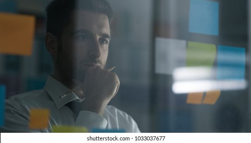 Business executive reading sticky notes on a glass, he is thinking about creative business solutions and strategies