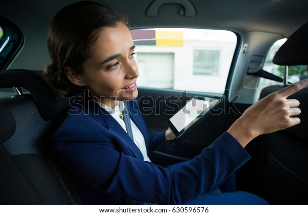 Business executive using digital tablet while\
traveling in car