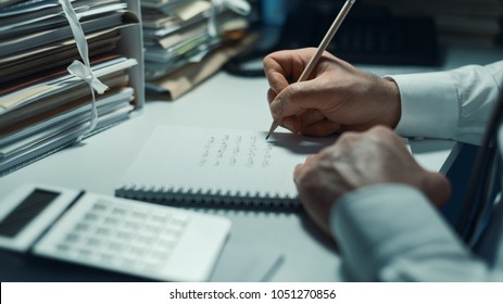 Business Executive Working Overtime At Night In The Office, He Is Writing Notes And Calculating Costs