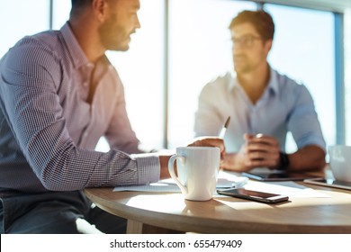 Business executives discussing work at office. Closeup of coffee cup with blurred image of two businessmen sitting on table.