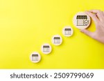 Business expansion and franchise growth concept. Hand selecting large store icon among smaller ones on yellow background, symbolizing franchise business growth, expansion strategy, market selection,