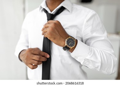 Business And Fashion. Closeup Cropped View Of Unrecognizable Young African American Businessman Adjusting Necktie At Home, Getting Ready For Work, Wearing White Shirt And Luxury Watch