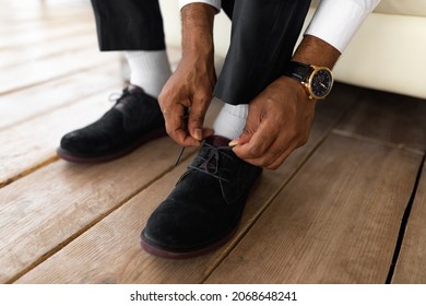 Business And Fashion. Closeup Cropped View Of Unrecognizable Young African American Businessman Putting On Shoes And Tying Laces At Home, Getting Ready For Work, Wearing Suit And Luxury Watch