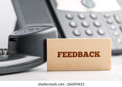 Business Feedback Concept With A Small Card With The Text - Feedback - Propped Against The Handset Of A Land Line Telephone That Is Lying On A White Table Off The Hook.