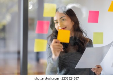 Business female employee with many conflicting priorities arranging sticky notes commenting and brainstorming on work priorities colleague in a modern office. - Powered by Shutterstock