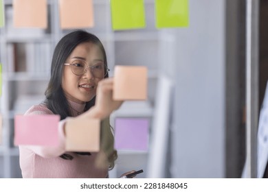 Business female employee with many conflicting priorities arranging sticky notes commenting and brainstorming on work priorities colleague in a modern office.
 - Shutterstock ID 2281848045