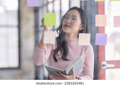 Business female employee with many conflicting priorities arranging sticky notes commenting and brainstorming on work priorities colleague in a modern office.
 - Shutterstock ID 2282265481