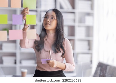 Business female employee with many conflicting priorities arranging sticky notes commenting and brainstorming on work priorities colleague in a modern office.
 - Shutterstock ID 2282265633