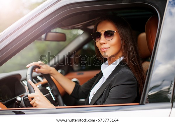 Business Female in a suit driving luxury car. Successful\
woman in the car salon holding hands on the steering wheel. Vintage\
filter. Beautiful young woman looking out the window Car     \
