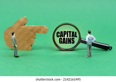 Business and finance concept. On the green surface there is a figure of a hand, miniature figures of people and a magnifying glass with the inscription - Capital Gains