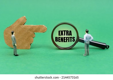 Business and finance concept. On the green surface there is a figure of a hand, miniature figures of people and a magnifying glass with the inscription - Extra Benefits - Shutterstock ID 2144573165
