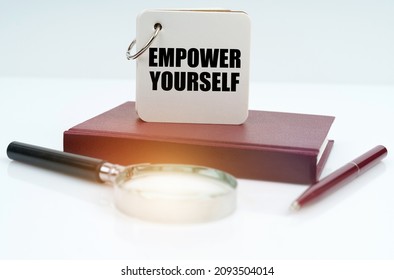 Business and finance concept. On a white surface lies a red notebook and pen, a magnifying glass and a white notebook with the inscription - Empower Yourself