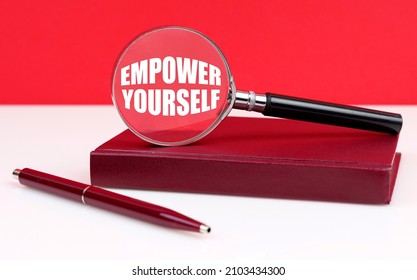 Business and finance concept. On a white and red background, a notebook, a pen and a magnifying glass, inside which the inscription - EMPOWER YOURSELF