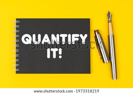 Business and finance concept. On a yellow background lies a pen and a black notebook with the inscription - Quantify It