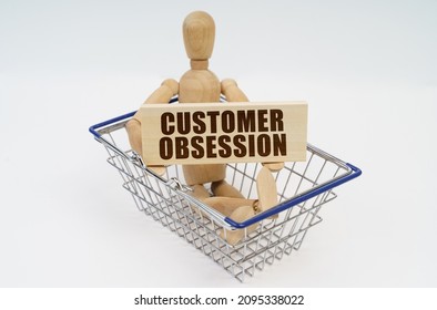 Business And Finance Concept. A Wooden Man Sits In A Shopping Basket, Holding A Sign In His Hands - Customer Obsession