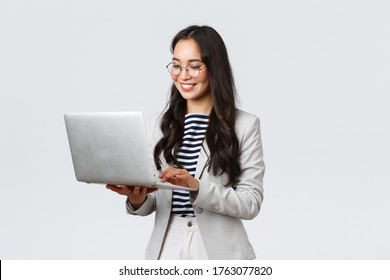 Business, Finance And Employment, Female Successful Entrepreneurs Concept. Professional Stylish Asian Businesswoman Fixing Project On Her Way To Office, Using Laptop Standing Whtie Background