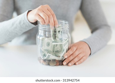 business, finance, saving, banking and people concept - close up of woman hands putting us dollar money into glass mason jar