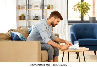business, finances, accounting and people concept - man with calculator counting and filling papers at home