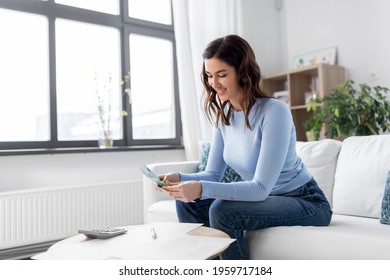 Business, Finances, Income And People Concept - Happy Smiling Woman With Calculator And Bills Counting Money At Home