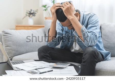Business financial concept, owe asian young man, male sitting on sofa expression face stressed by calculate expense on table from invoice or bill have no money to pay mortgage or loan, debt bankruptcy