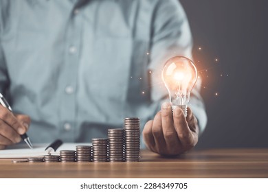Business, Financial and money planning idea, Clever thinking about money saving for future, Man calculating number of money, increasing coin stacked and holding light bulb on the table. Studio shot. - Shutterstock ID 2284349705