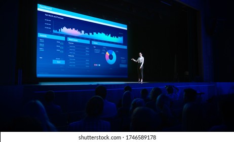 Business Forum Economics Conference Stage: Visionary Female Chief Analyst Delivers Speech And Shows Infographics, Statistics On Movie Theater Screen. Presentation With Speaker In Full Auditorium Hall