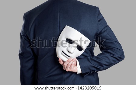 Business fraud concept. Businessman hide the mask in hand behind his back. 