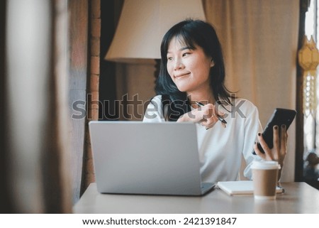 Business freelance concept, Pensive young Asian woman gazing away while working on a laptop and holding a smartphone in a well-lit room.

