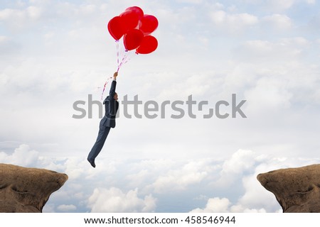 business gap concept businessman flying over a crevasse using helium balloons