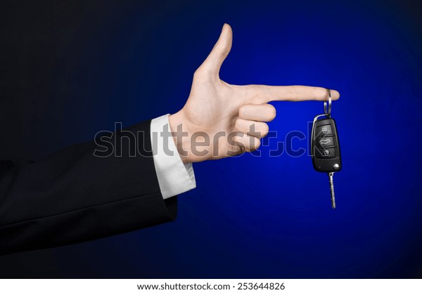 Business and\
gift theme: car salesman in a black suit holds the keys to a new\
car on a dark blue background in\
studio