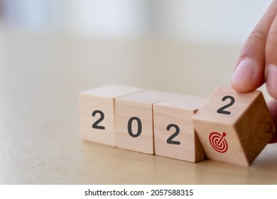 Business goals in 2022 concept. Businessman hand flips wooden cubes "2022" and "dart board has dart arrow hitting" icon on beautiful  background and copy space. For starting business plan next year.