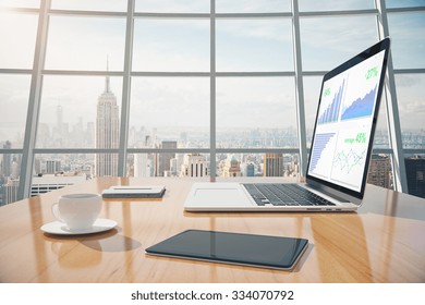 Business graphs on laptop screen, coffee mug, digital tablet on the table in sunny office with windows in floor - Powered by Shutterstock