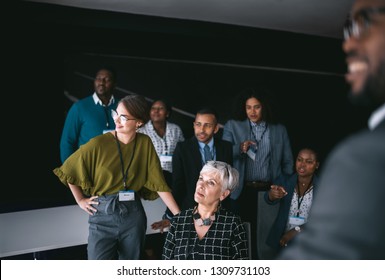 Business Group Having A Discussion, Looking And Pointing To A Large Video Wall With Charts And Graphs Out Of Frame