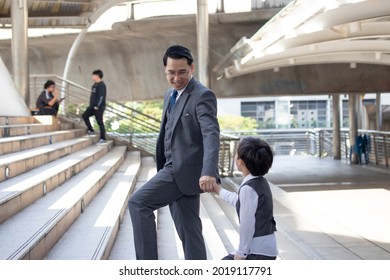 Business And Grow Up Concept. Business Father Holding His Son Hand Walking Up Stairs Going To Work At Morning In The City.