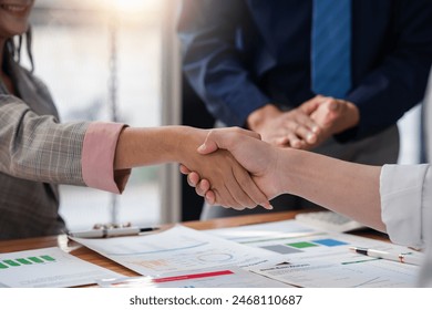 Business handshake between two professionals sealing a deal with papers and charts on the table, indicating successful partnership. - Powered by Shutterstock