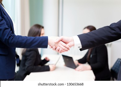 Business Handshake At The Office With Bussiness People On Background