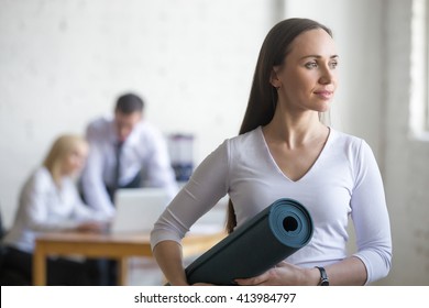 Business and healthy lifestyle concept. Portrait of beautiful sporty young office woman standing with yoga mat at workplace on break time - Powered by Shutterstock