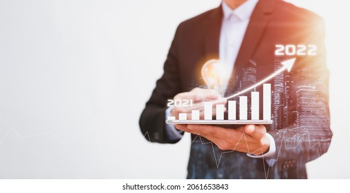 Business holding light bulb with growth data chart arrow with diagram 2022 budget, Businessman pointing arrow graph corporate future growth year 2021 to 2022, Development to success and motivation.
