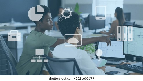 Business icons image over diverse professionals working on computers in office. teamwork, collaboration, technology, workplace, brainstorming, digital - Powered by Shutterstock