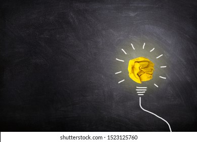 Business Idea Concept : Yellow crumpled paper ball light bulb lighting grow around on chalkboard.