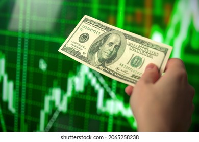 Business Investment And Stock Market. Hand Holding Dollars Banknote On Green Stock Chart Financial Graphs Background. Economic Growth, Currency Exchange Concept