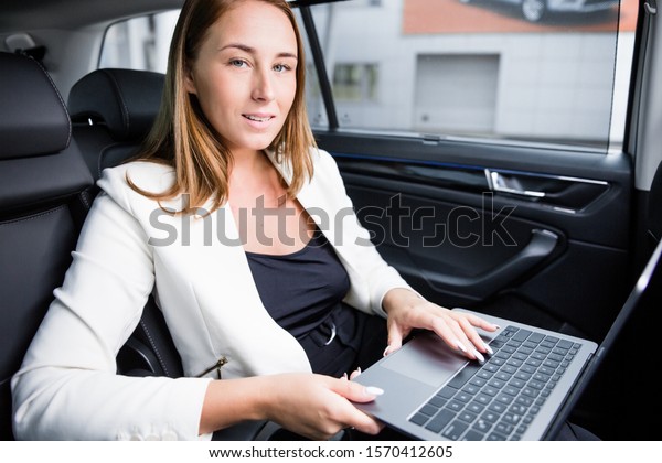 Business lady working on a laptop sitting in\
the back seat of the car. Remote\
work