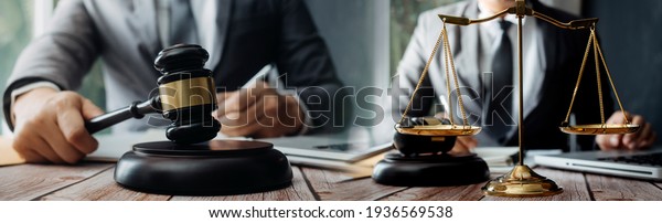 Business and lawyers\
discussing contract papers with brass scale on desk in office. Law,\
legal services, advice, justice and law concept picture with film\
grain effect