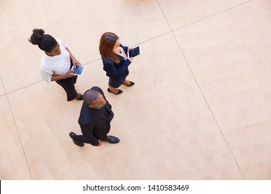 Business Leader And His Female Assistants Walking Through Office Lobby. Top View Of Mix Raced Team Of People In Formal Clothes Using Tablets And Discussing Project. Businesspeople Concept