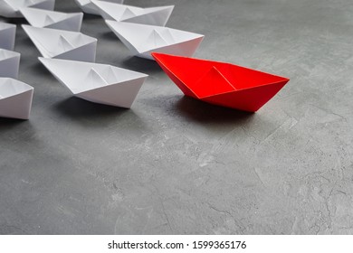 Business Leadership Concept, Paper Boat, The Key Opinion Leader, The Concept Of Influence. One Red Paper Boat As The Leader, Leading In The Direction Of The White Ships On A Gray Concrete Background